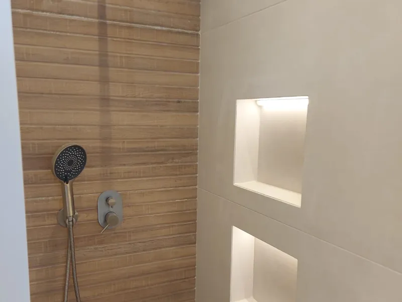 מקלחת עם ראש גשם, מקלחון יד ונישות מוארות בקיר — עבודה של דניאל